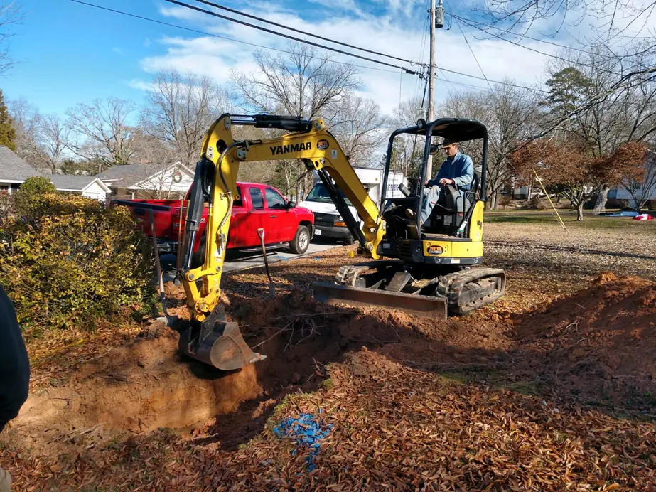 A Fortune Plumbing technician running a mini excavator along an open trench on a North Georgia property
